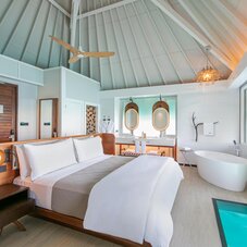 Elegant overwater bungalow bedroom at The Westin Bora Bora featuring a comfortable bed, contemporary island décor, and views of the turquoise lagoon through the open windows.